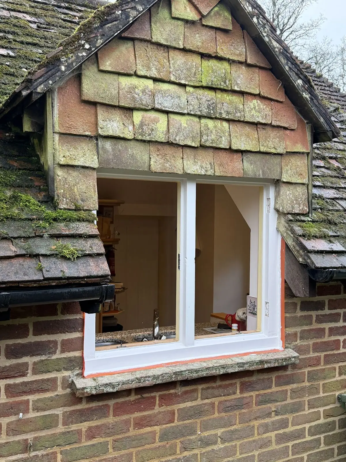 Sash window reinstalled in a tile-hung dormer with the brush-pile seal fitted; fresh paint and masking tape on the reveal