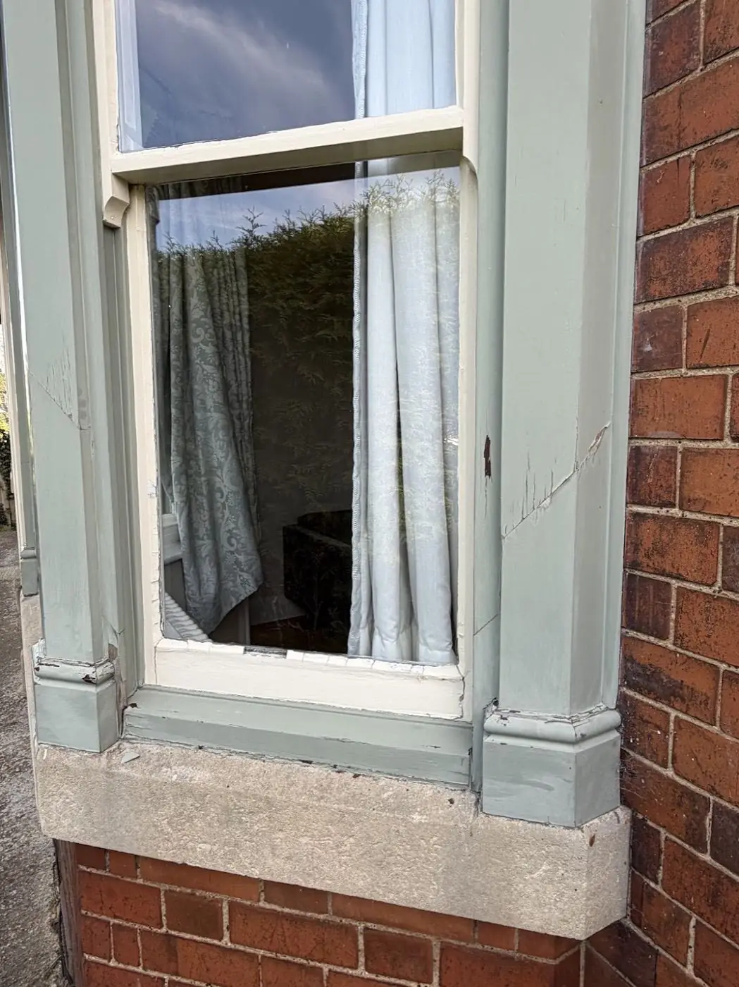 Sash window before refurbishment — pale-green peeling paint, weathered timber, lace curtains visible