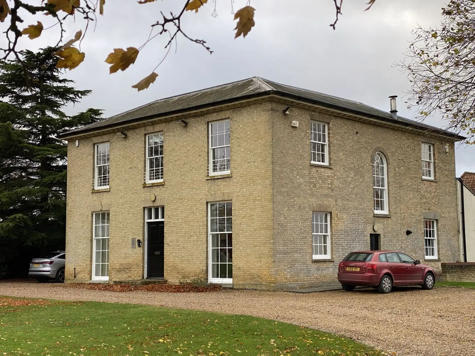 A Suffolk period house near Newmarket — three storeys, white-painted sash windows on a pale stock-brick façade, hipped roof, gravel drive