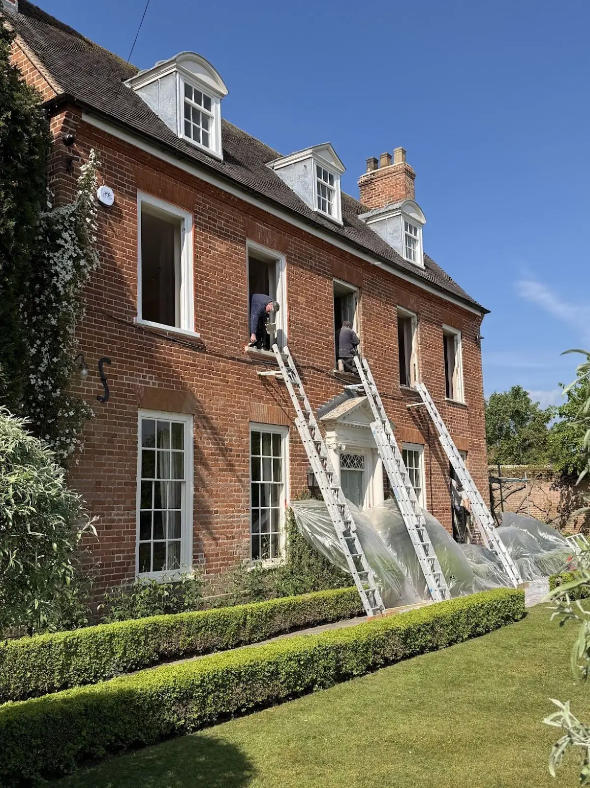 Restoration crew working on upper-floor sash windows of a Georgian brick house