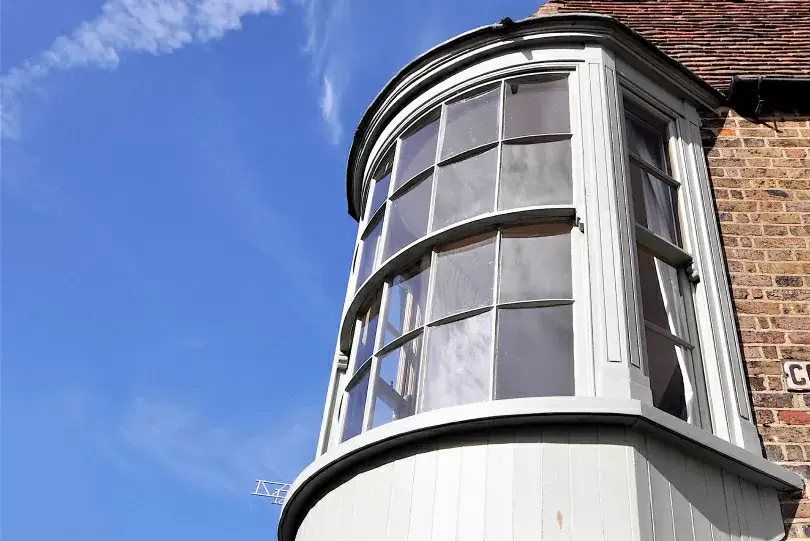 A round bay window with white frames and a hint of classic sash window styles protrudes from a brick wall under a clear blue sky.