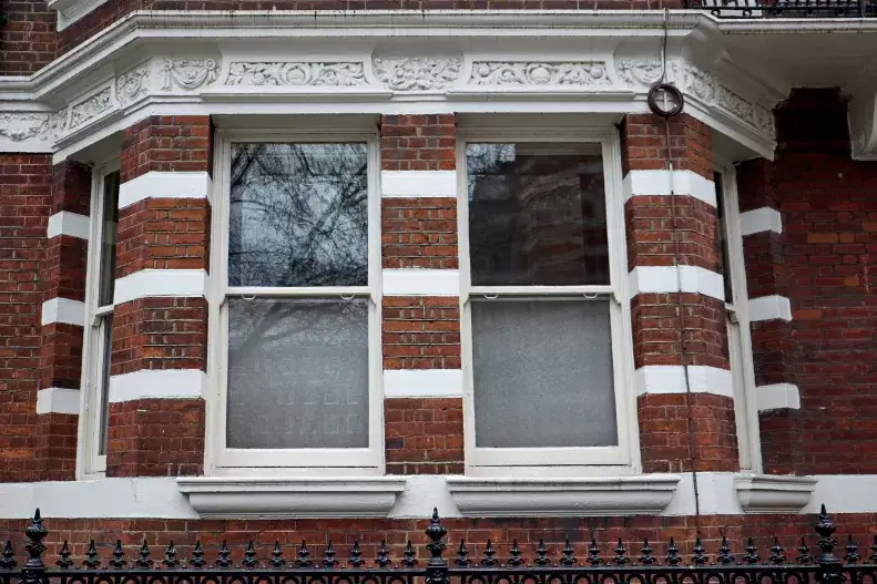 Red brick building with white decorative accents, featuring two large sash windows with partially frosted glass—a nod to the history of sash window styles. Black iron fence in the foreground.