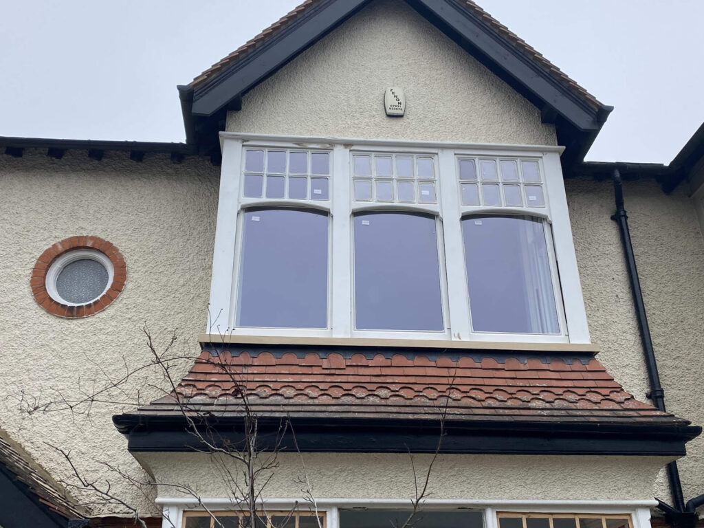 The exterior view of this Barnet house showcases three large sash windows with double glazing on the upper floor, complemented by a circular window on the side and a classic red-tiled roof.