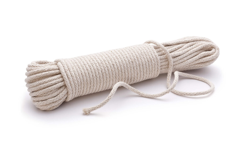 A neatly coiled bundle of beige rope, resembling traditional sash cords, with a loose end rests on a white surface.